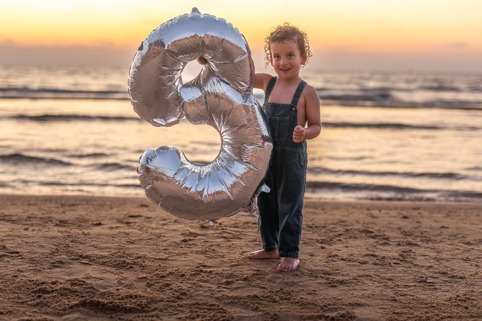 פעוט לצד בלון ענק בצורת 3 על החוף בשקיעה
