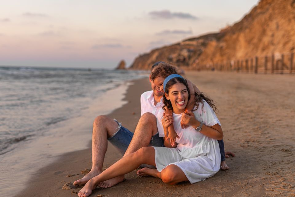 הורים וילד מחובקים על החול בשקיעה